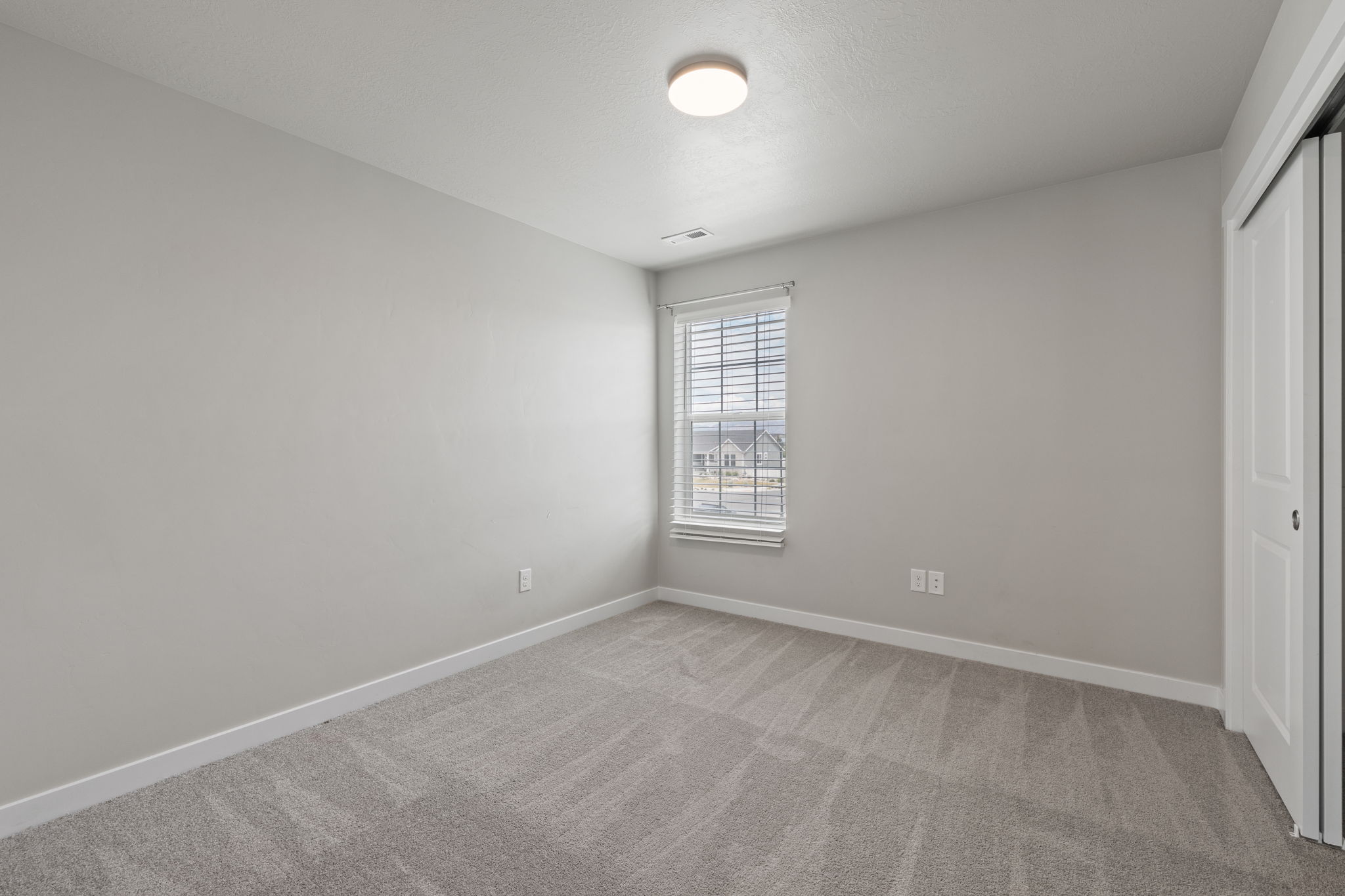 Carpeted room with a window featuring blinds, a flush mount ceiling light, and bi-fold closet doors