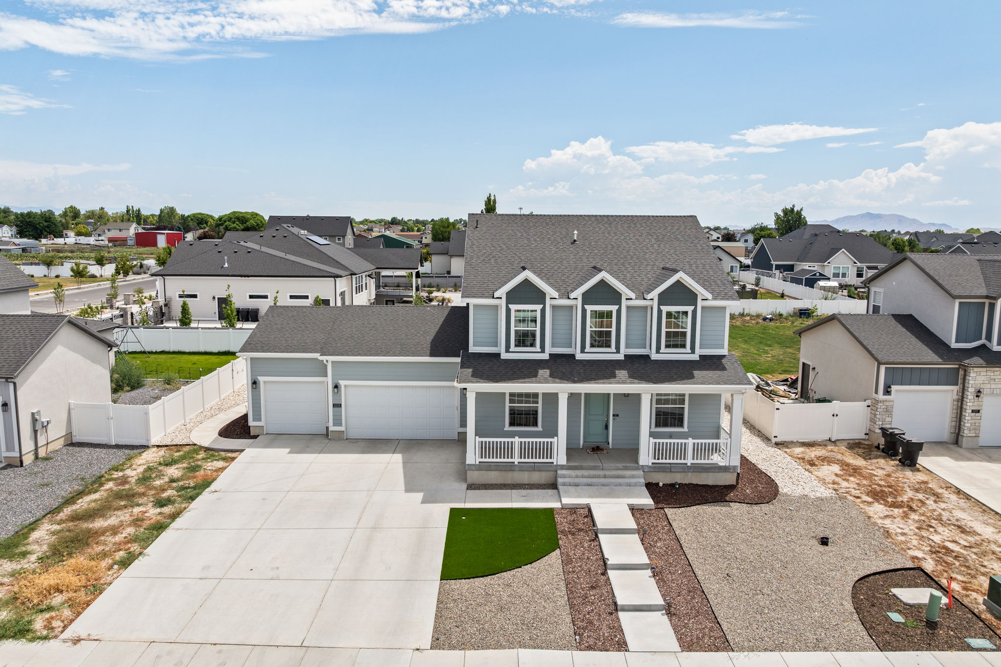 Contemporary two-story home featuring a three-car garage, a covered front porch with white railings, and a light blue exterior with dark gray accents