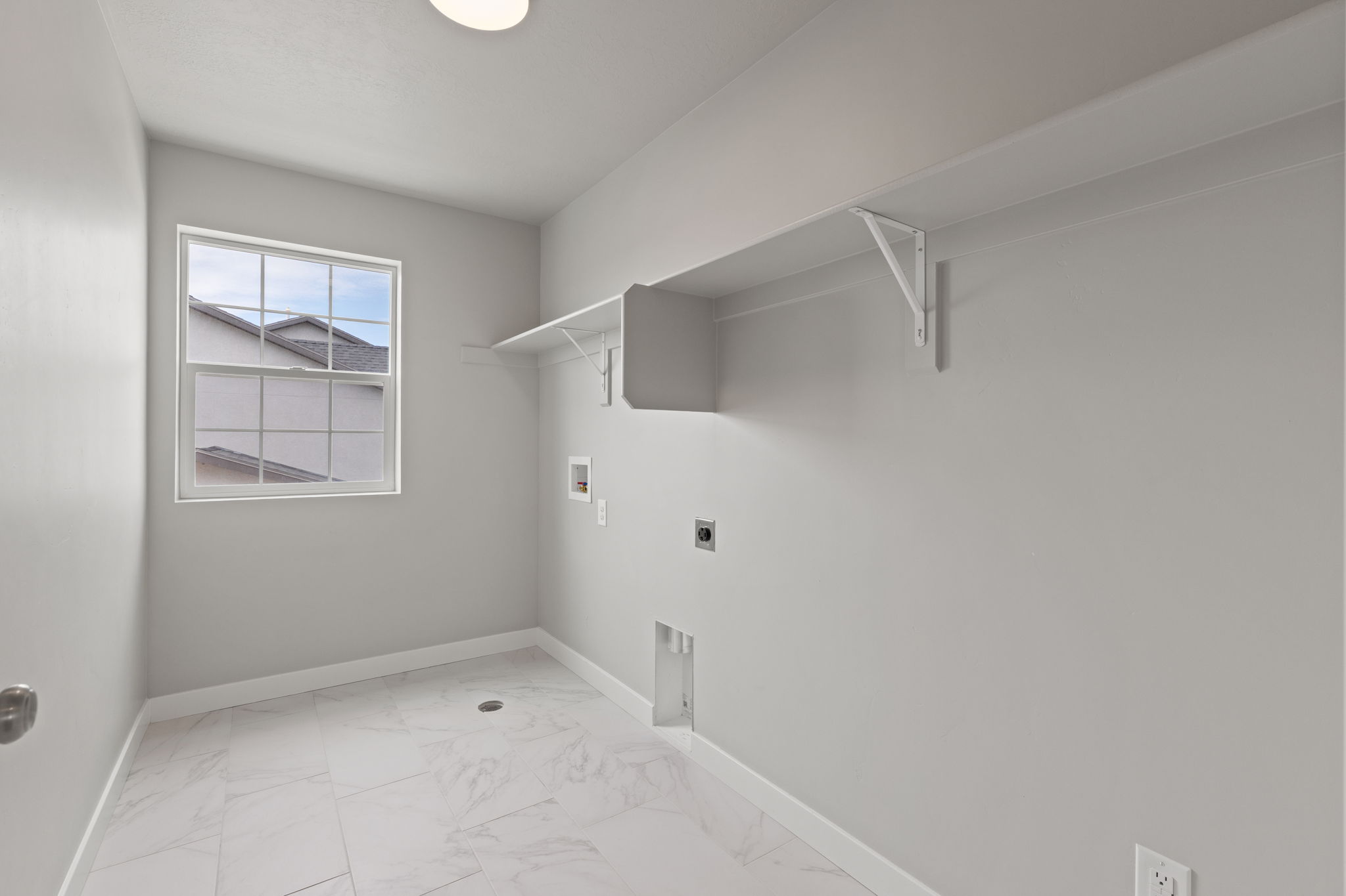 Utility room featuring a window, overhead shelving, and white tile flooring