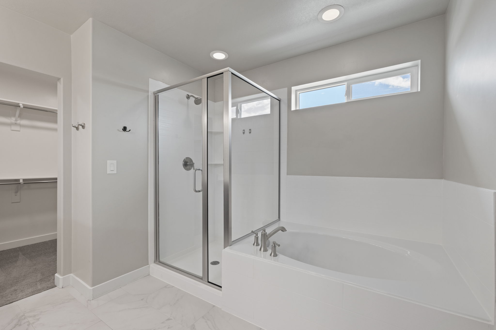 Bathroom featuring a glass-enclosed shower, built-in soaking tub with deck-mounted fixtures, marble-finish floor tiling, and a high horizontal window