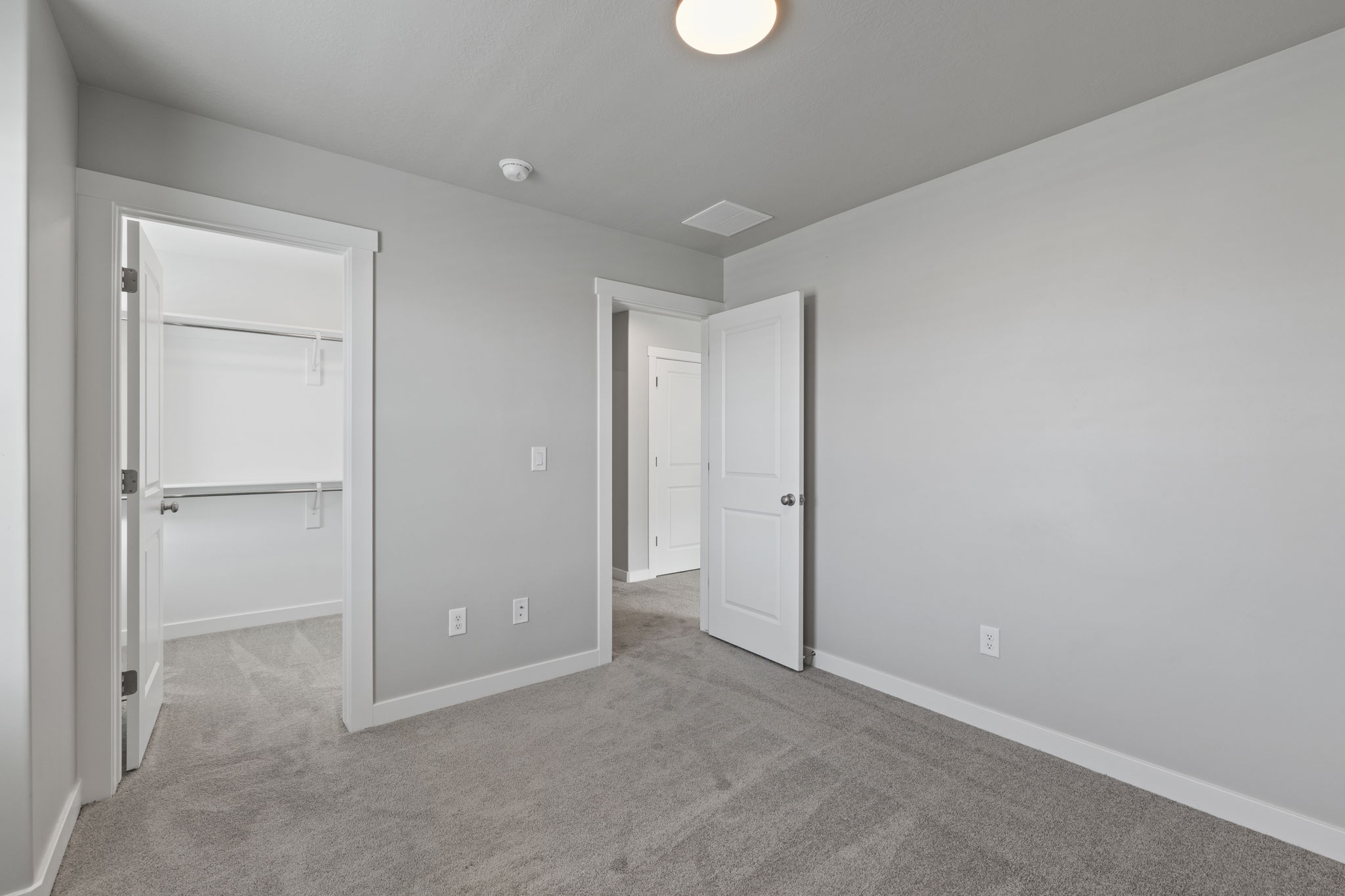 Spacious room featuring light gray wall paint, plush gray carpeting, white trim, and a white two-panel interior door