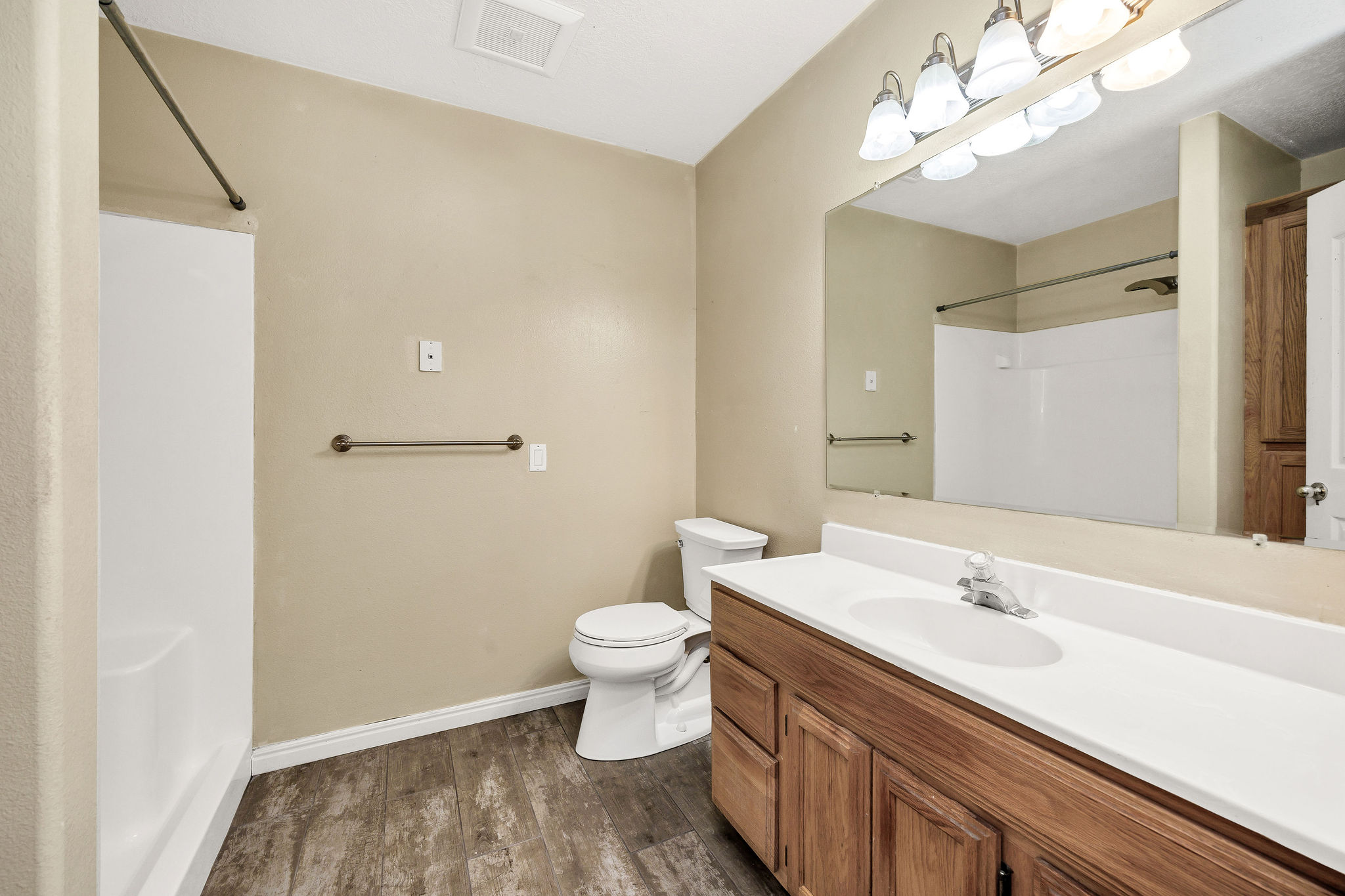 Bathroom featuring a wood-finish vanity with a white countertop and integrated sink, a large wall-mounted mirror, and a combination tub/shower