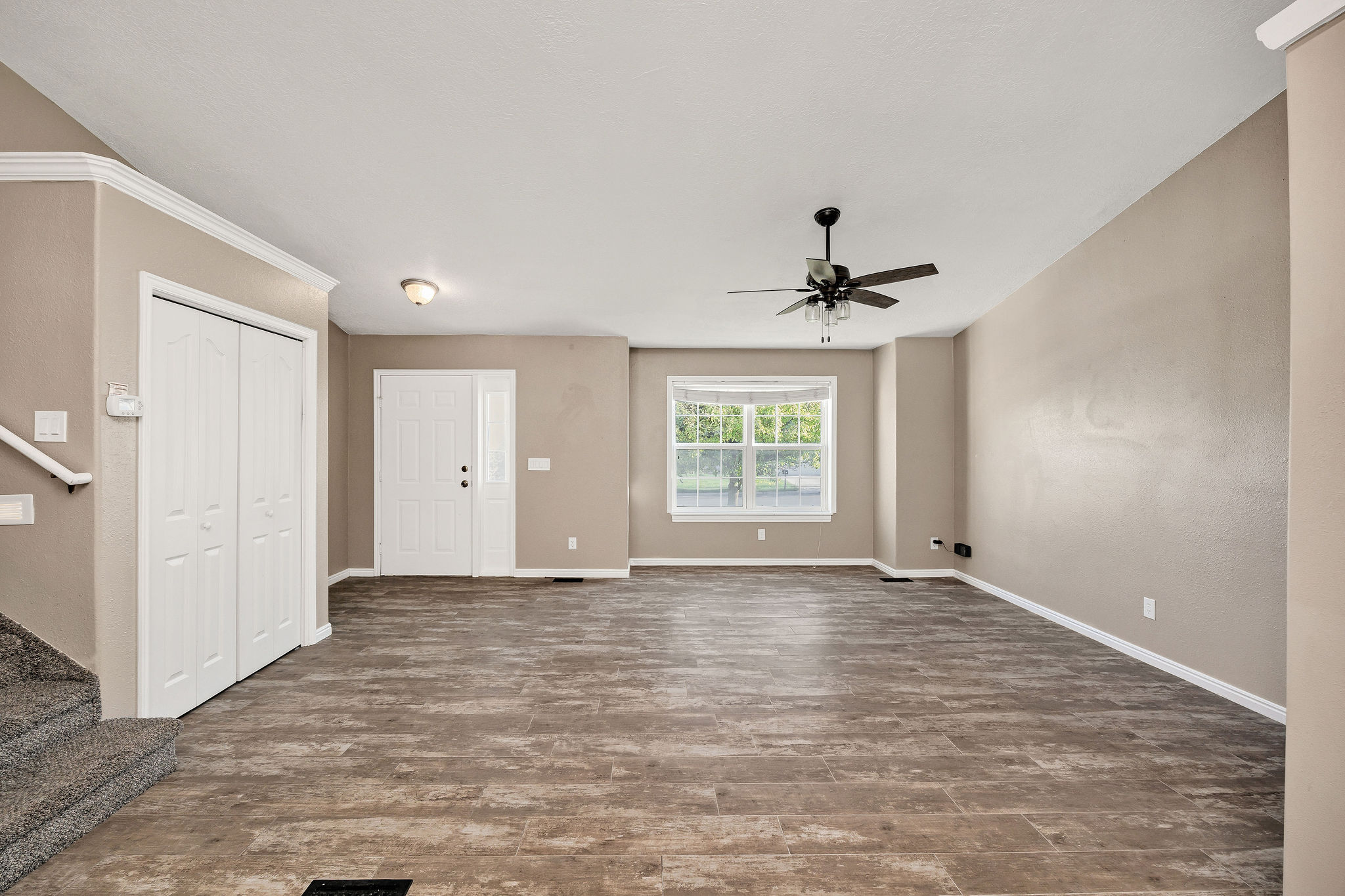 Spacious entry and living area featuring wood-finish flooring, a contemporary ceiling fan, and a double front door with sidelight