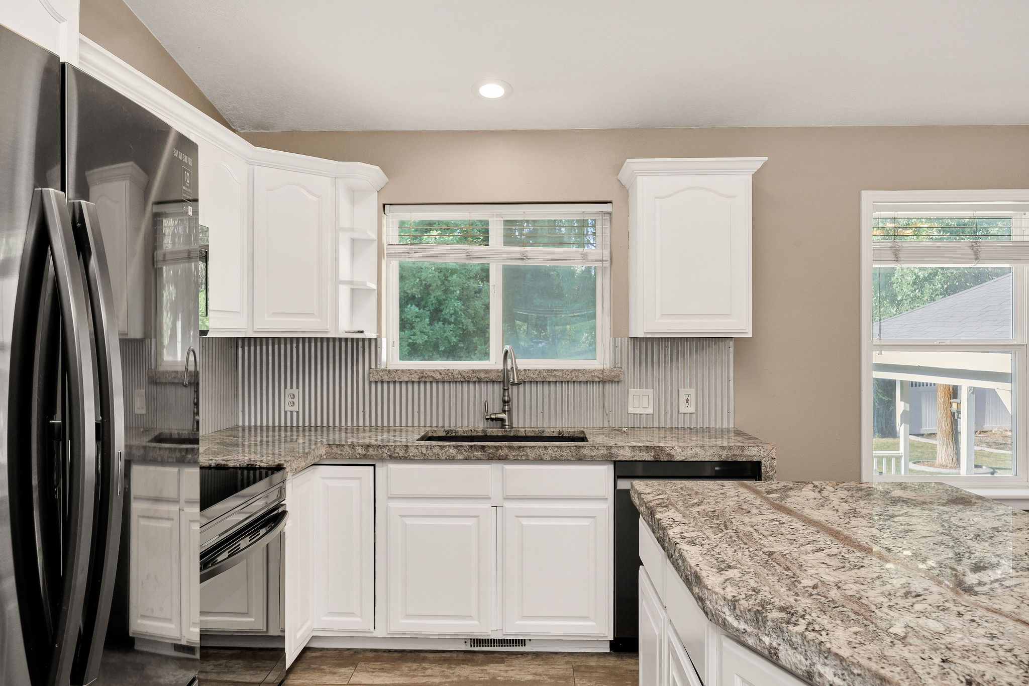 Kitchen with white cabinetry, granite countertops, and a corrugated metal backsplash
