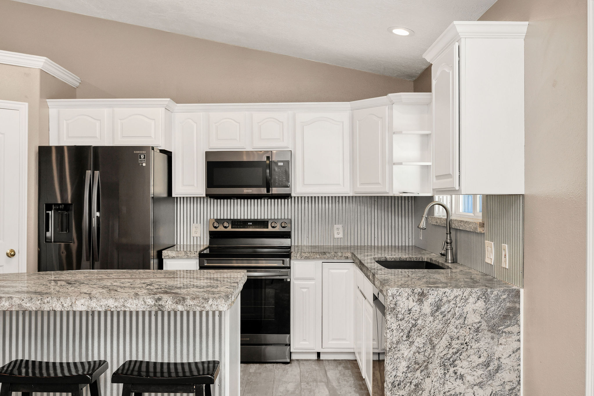 Kitchen featuring white cabinetry, stone countertops, stainless steel appliances, a bar seating area, and wood-finish flooring