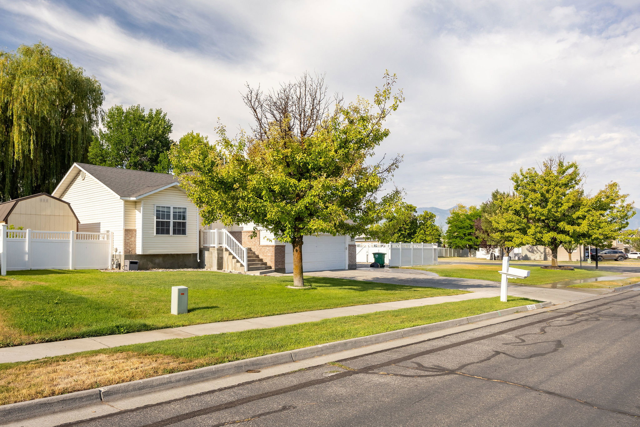 Suburban residence featuring a white vinyl fence, attached garage, and mature trees