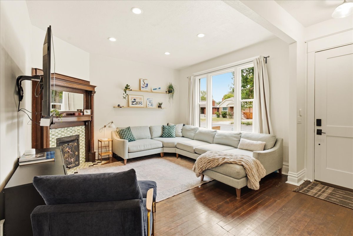 Living area featuring rich wood-finish flooring, a decorative fireplace with a wood mantle and tiled surround, recessed lighting, and a large picture window