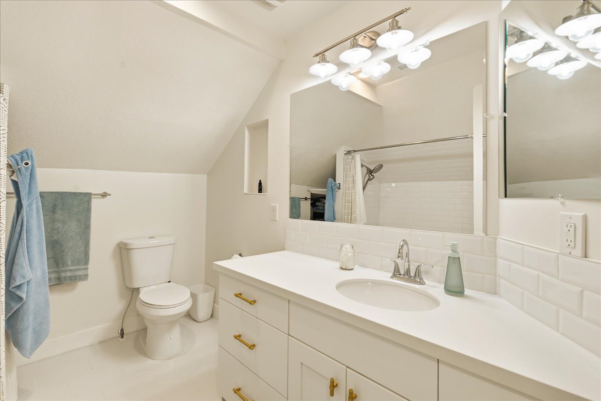 Contemporary bathroom featuring a white vanity with gold-tone hardware, a white countertop with an integrated sink, a large mirror, and subway tile backsplash