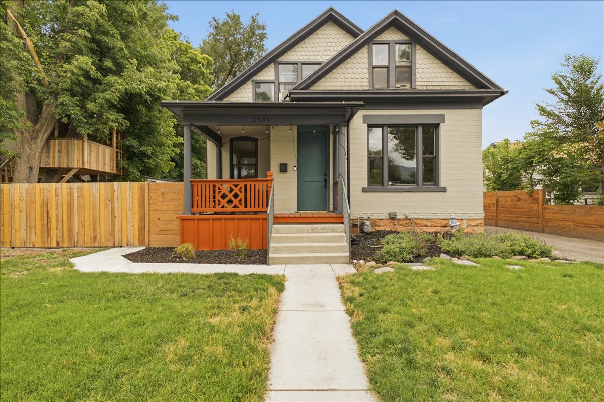 Gabled architectural style featuring a covered porch with decorative railing, dark-trimmed windows, a teal entry door, and a manicured lawn