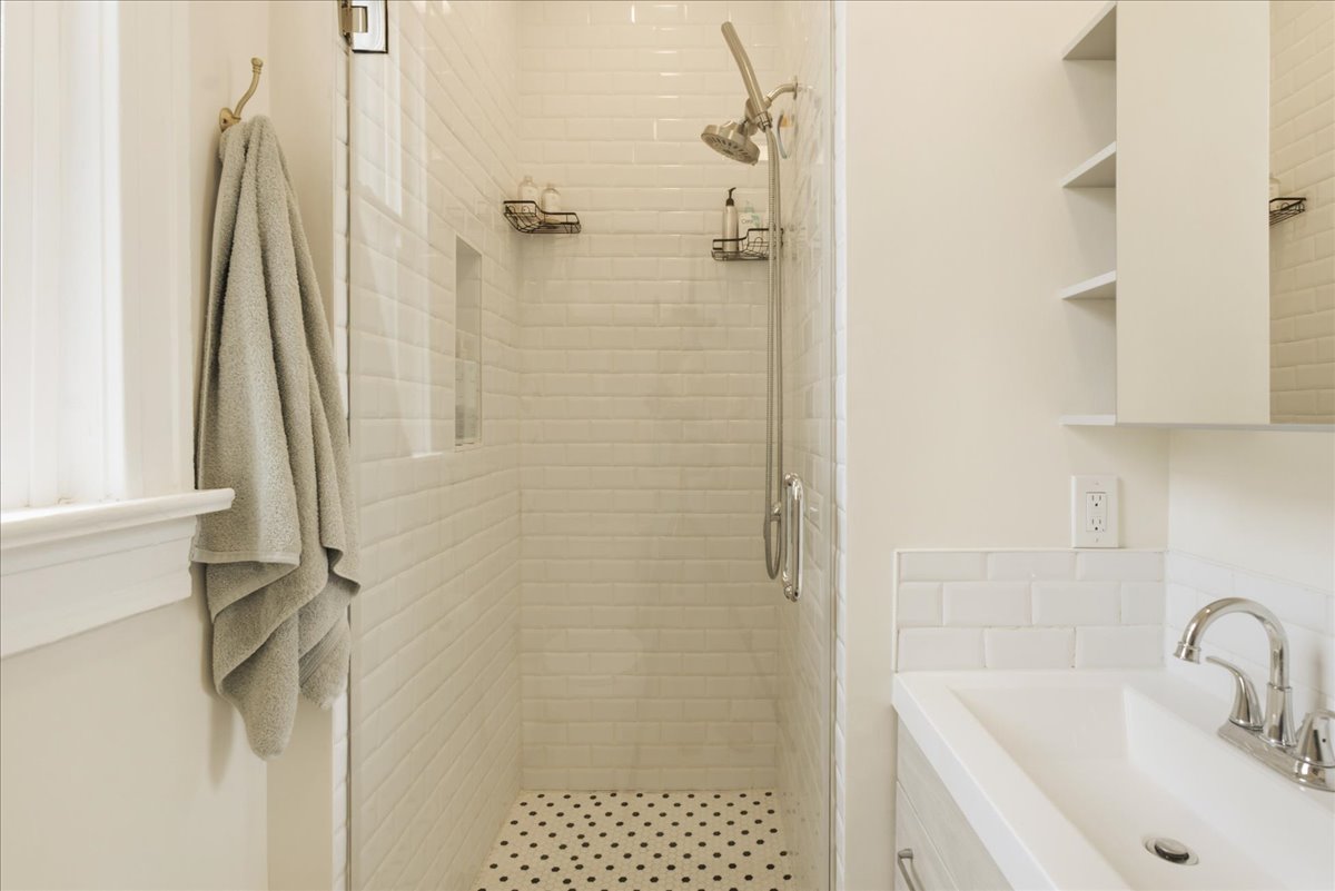 Shower with white subway tile surround and black and white penny tile flooring, featuring a built-in shower niche