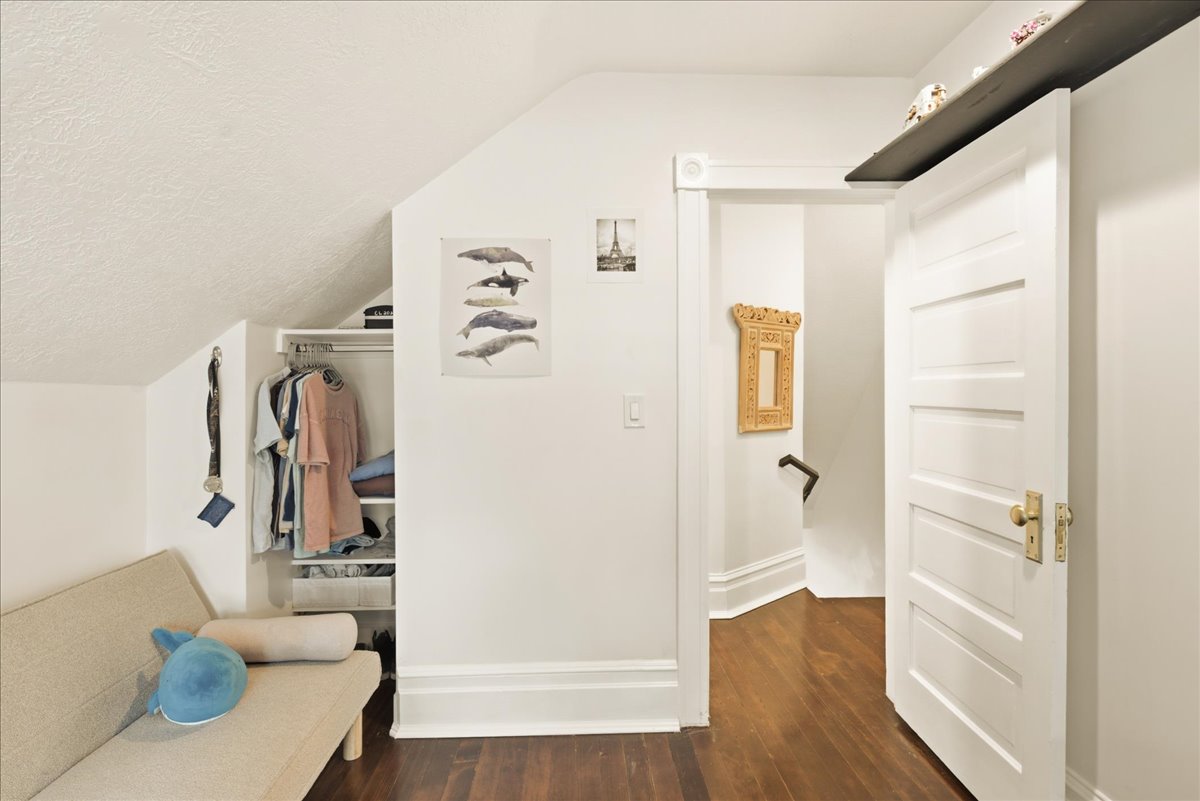 Attic room featuring rich wood-finish flooring, a built-in closet system, sloped ceiling, and white paneled door with brass hardware