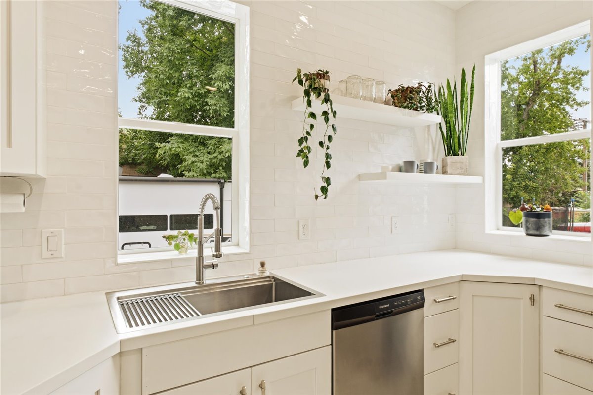 Kitchen featuring white shaker-style cabinetry, a stainless steel farmhouse sink with a gooseneck faucet, light-toned countertops, and a white subway tile backsplash