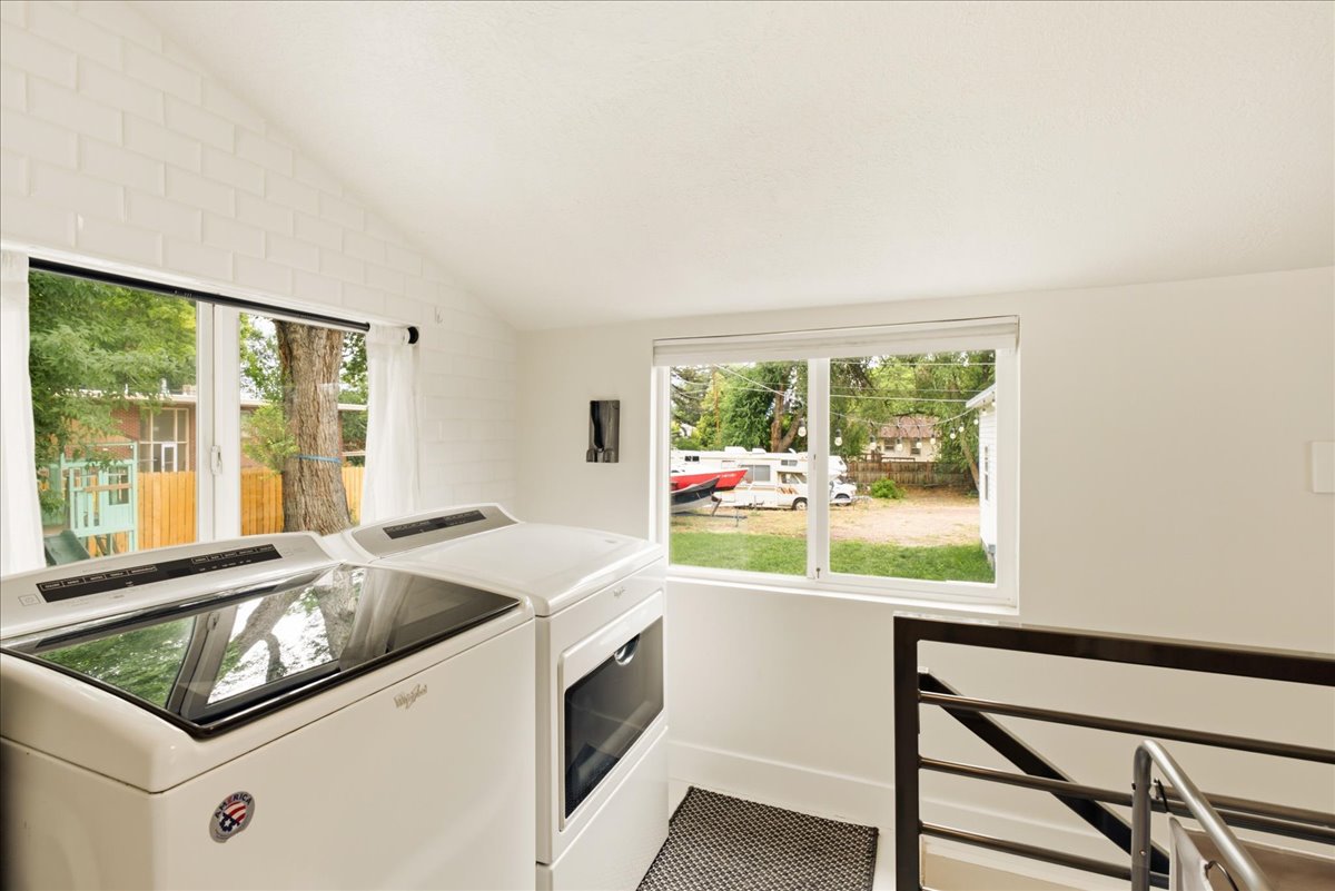Laundry area with vaulted ceiling, white painted brick accent wall, and dual pane windows