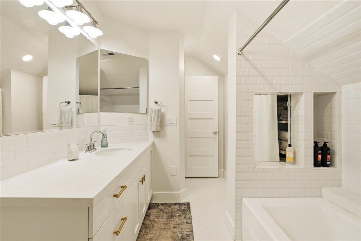 Spacious bathroom featuring a single vanity with a white countertop and gold-finish hardware, subway tile backsplash, recessed lighting, and a built-in shower niche