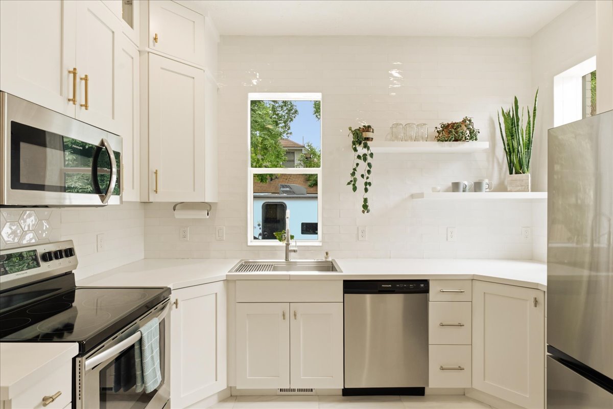 Modern kitchen featuring white cabinetry with gold-tone hardware, stainless steel appliances, white countertops, and a full-height tile backsplash