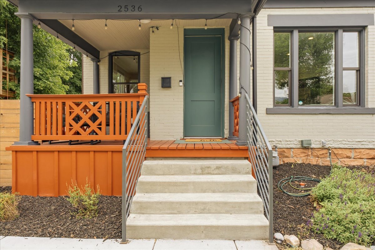 Inviting front porch with concrete steps, modern metal railings, a deep green entry door, and a decorative wood railing