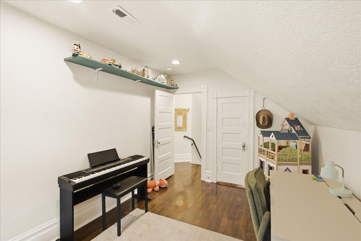 Attic room featuring rich wood-finish flooring, white walls, and a sloped ceiling