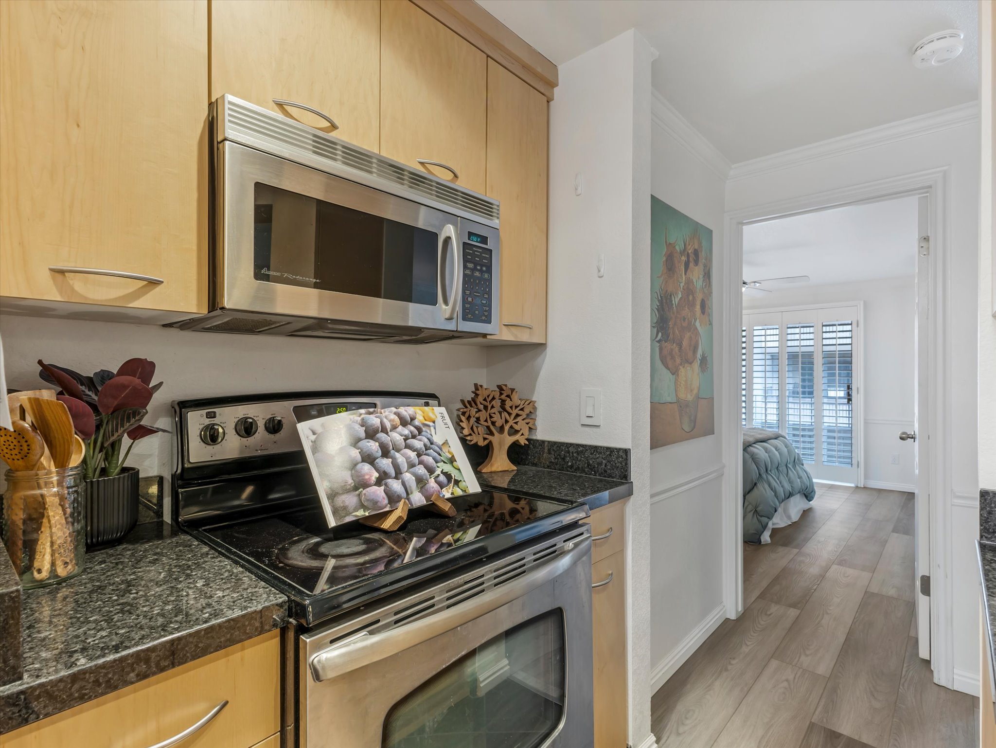 Kitchen featuring light wood-finish cabinetry with curved pulls, black granite-style countertops, and a stainless steel over-the-range microwave