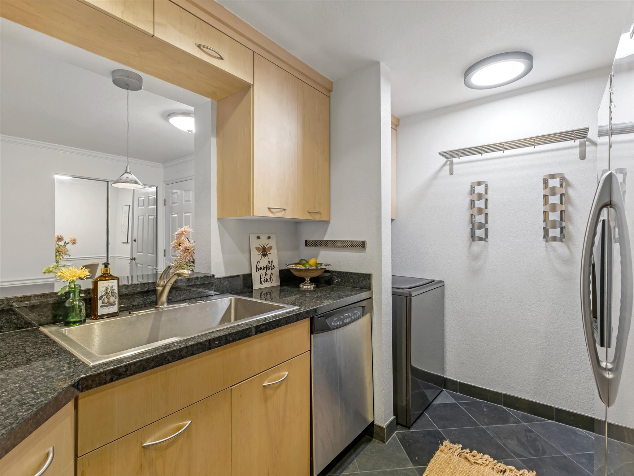Kitchenette featuring light wood-finish cabinetry, dark speckled countertops, and a stainless steel sink