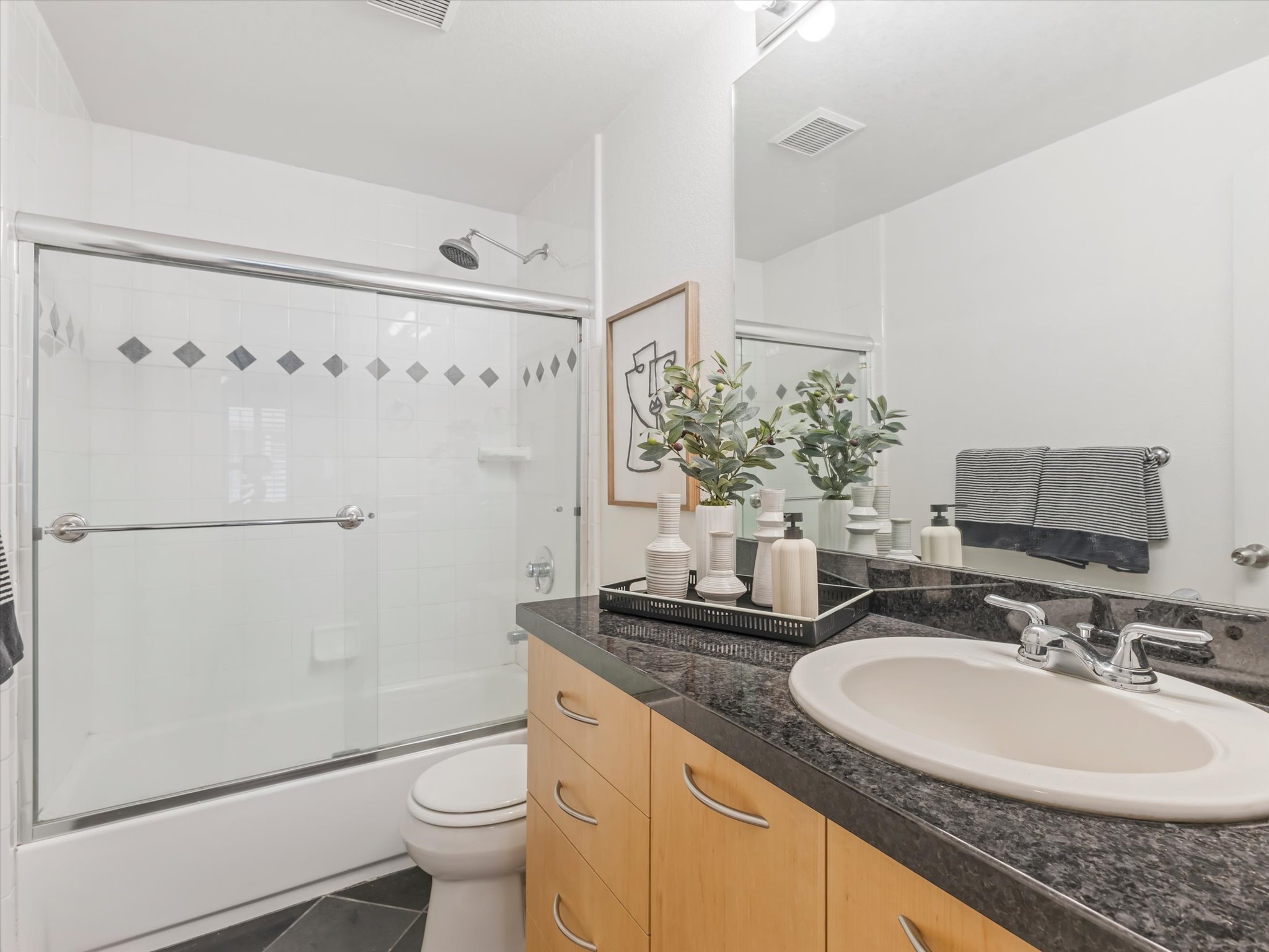 Bathroom featuring a vanity with a dark speckled countertop, light wood-finish cabinetry, and an undermount sink