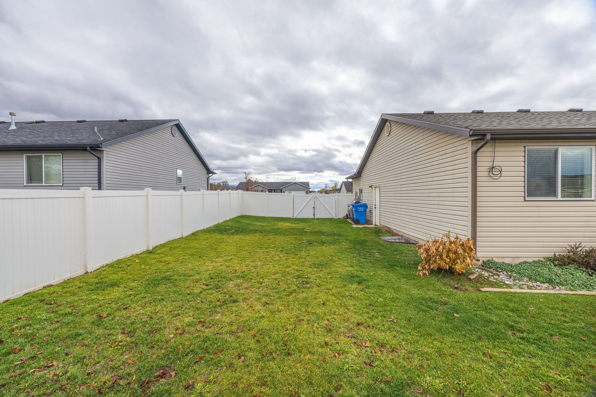 Expansive green lawn enclosed by a white vinyl privacy fence, with vinyl siding on the exterior