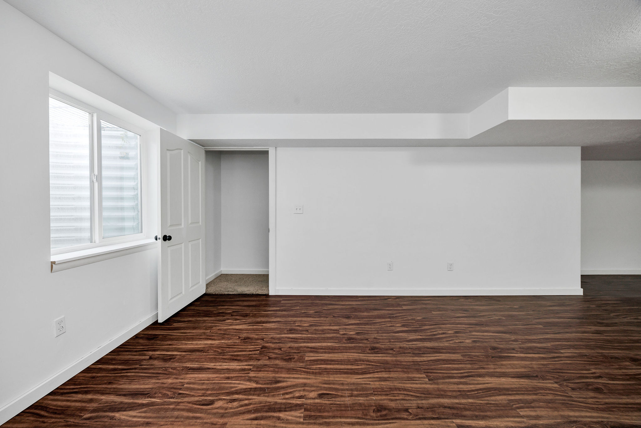 Spacious room featuring wood-finish flooring, white walls, and a white window with horizontal blinds