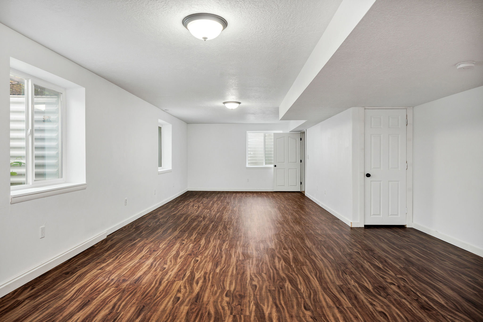 Spacious room featuring wood-finish flooring, white walls, and multiple windows