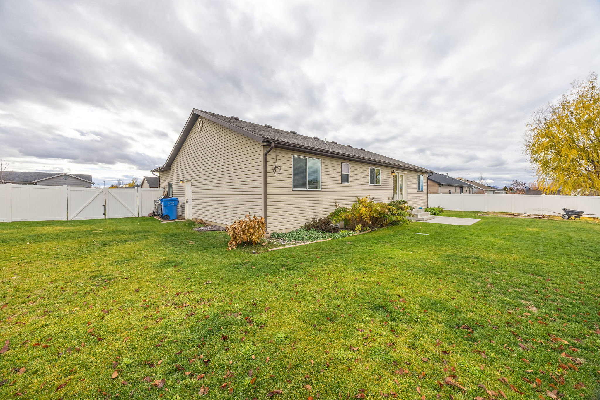 Expansive backyard featuring a lush lawn, white privacy fencing, and a concrete patio