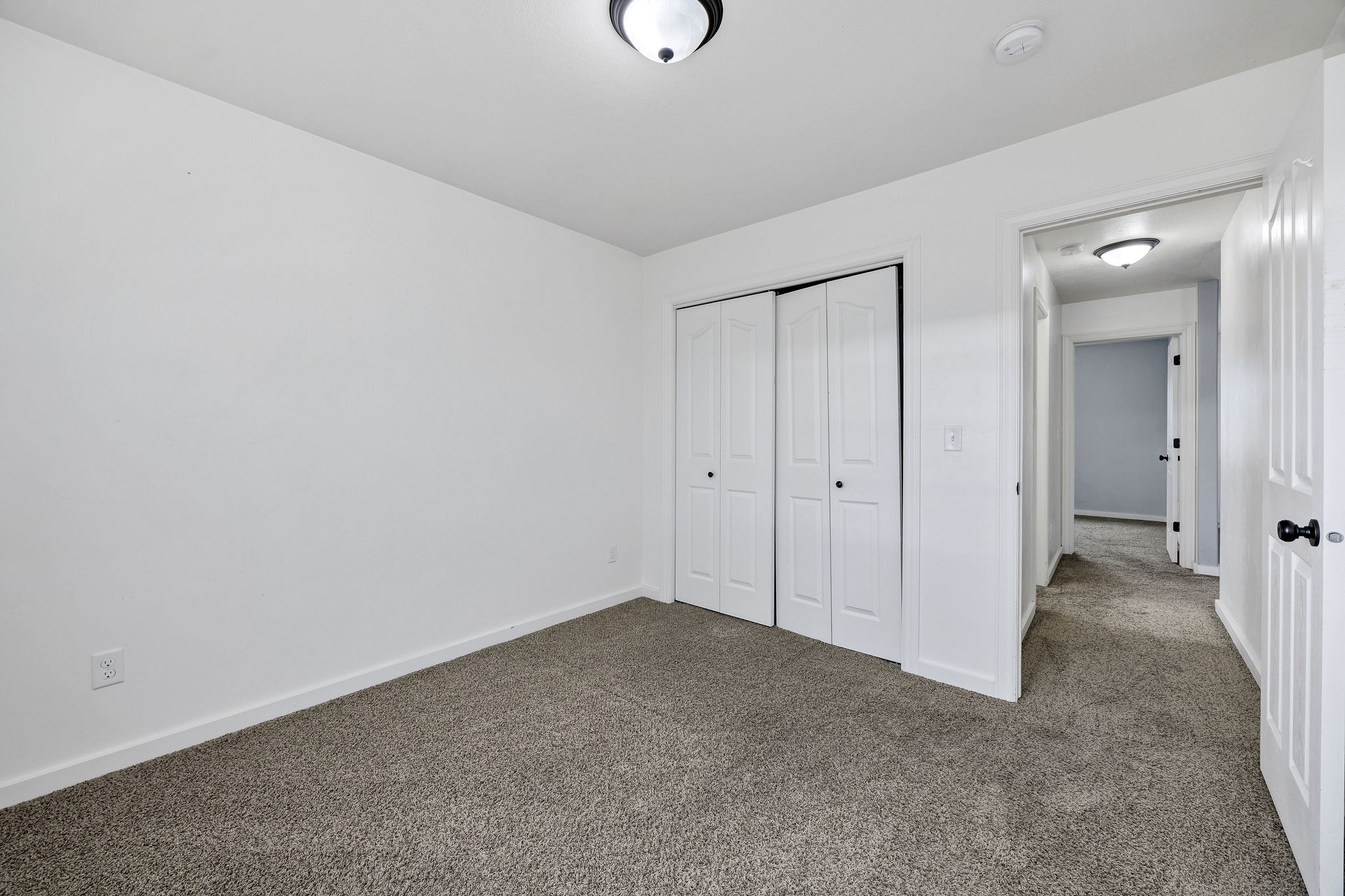 Neutral-toned carpet flooring and white walls define this space, featuring a double bi-fold closet