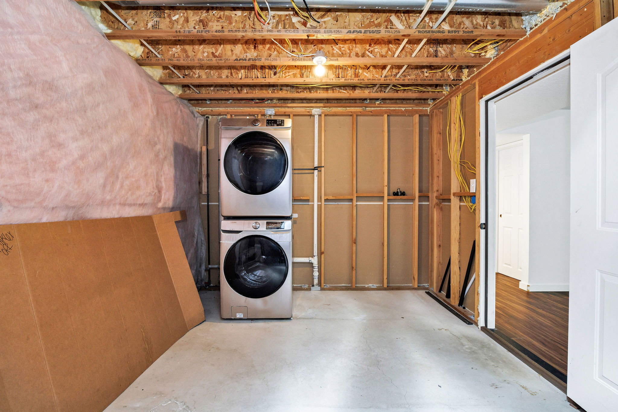 Laundry area featuring a stacked stainless steel washer and dryer, concrete flooring, and exposed ceiling joists