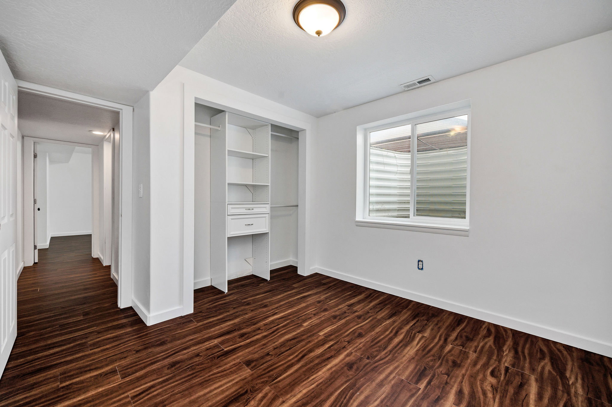Room featuring wood-finish flooring, a built-in closet system with shelving and drawers, white trim, and a window providing natural light