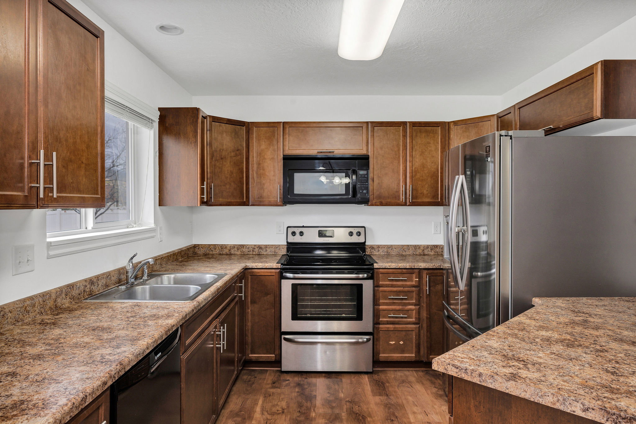 Kitchen featuring wood-finish cabinetry, patterned countertops, stainless steel appliances, and wood-finish flooring