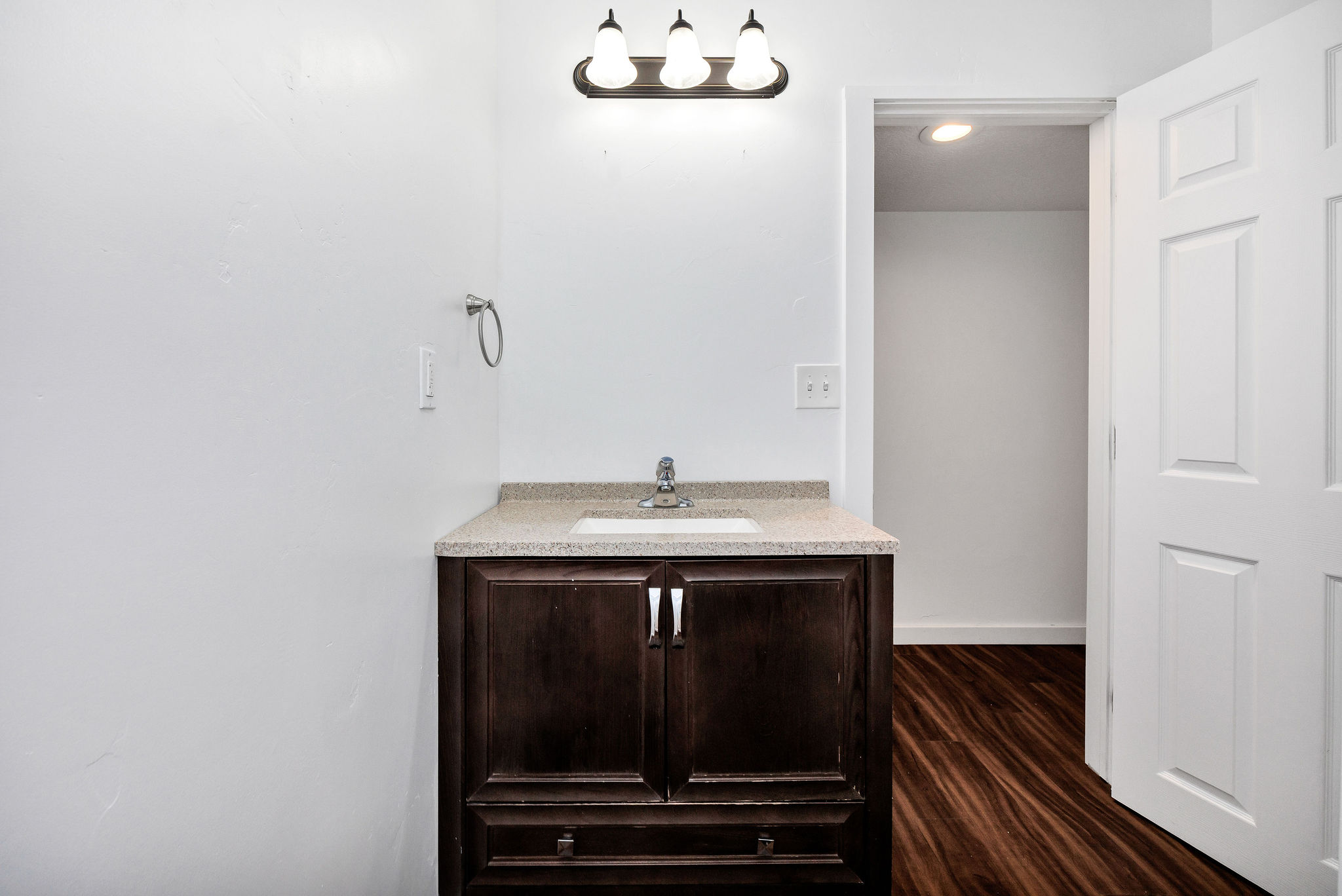 Bathroom vanity featuring a dark wood cabinet, light speckled countertop, and an integrated white sink with a chrome faucet