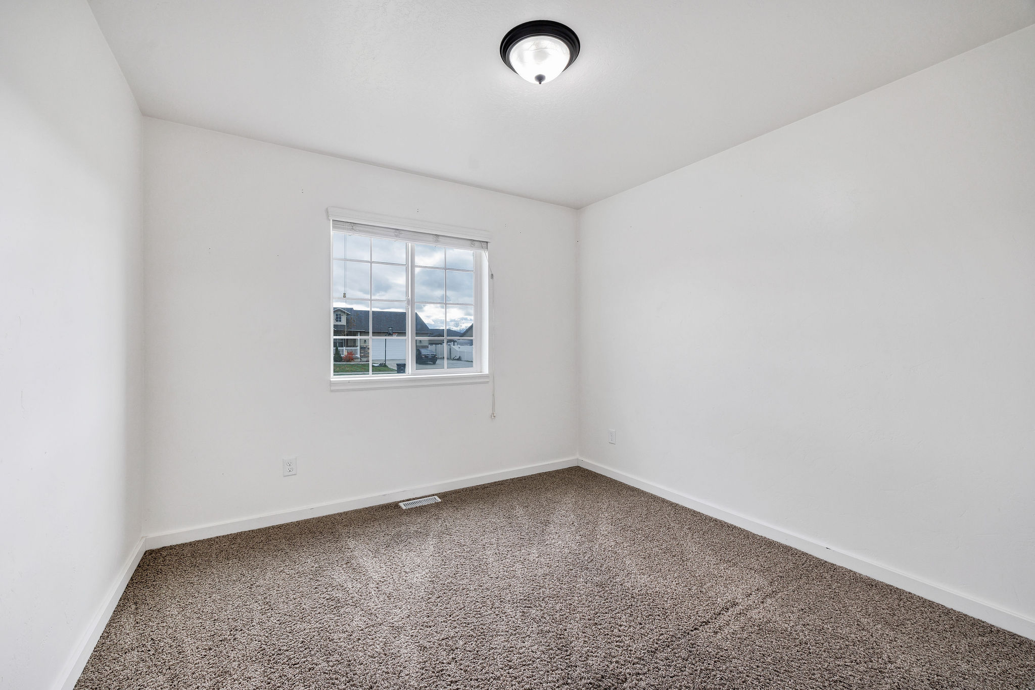 Carpeted room featuring a white-framed window, white walls, and a ceiling-mounted light fixture