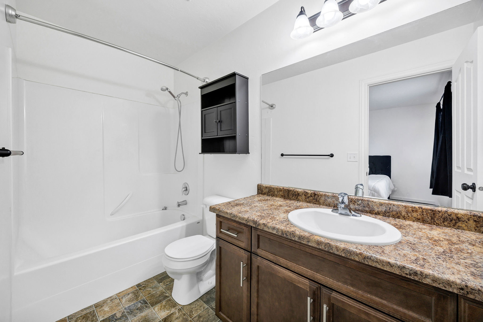 Bathroom featuring a dark wood finish vanity with a laminate countertop and integrated sink, a large wall-mounted mirror, and a white tub/shower combination with a chrome shower head