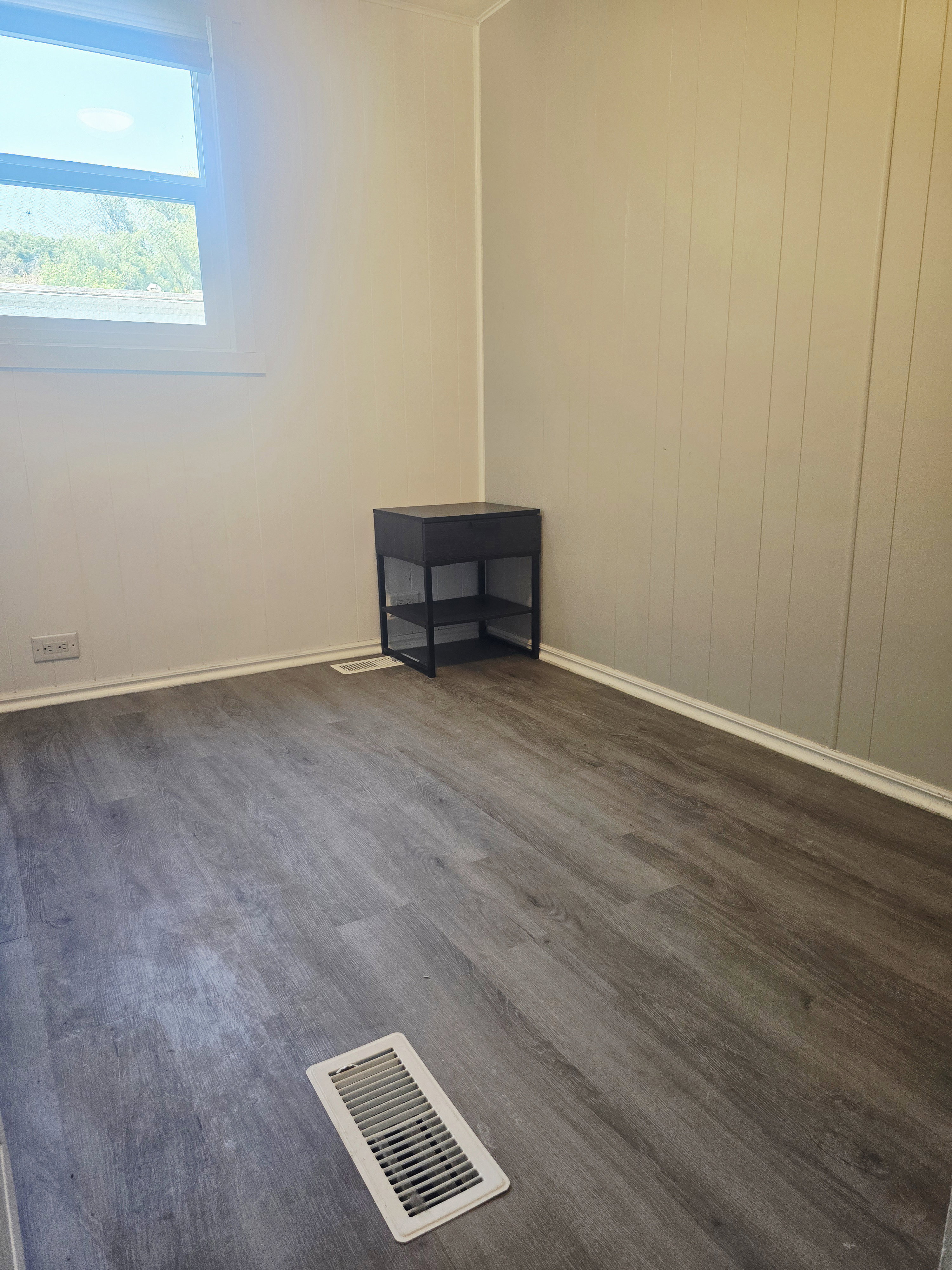 Light gray wood-finish flooring complements white baseboards and light-colored walls, one of which features vertical paneling