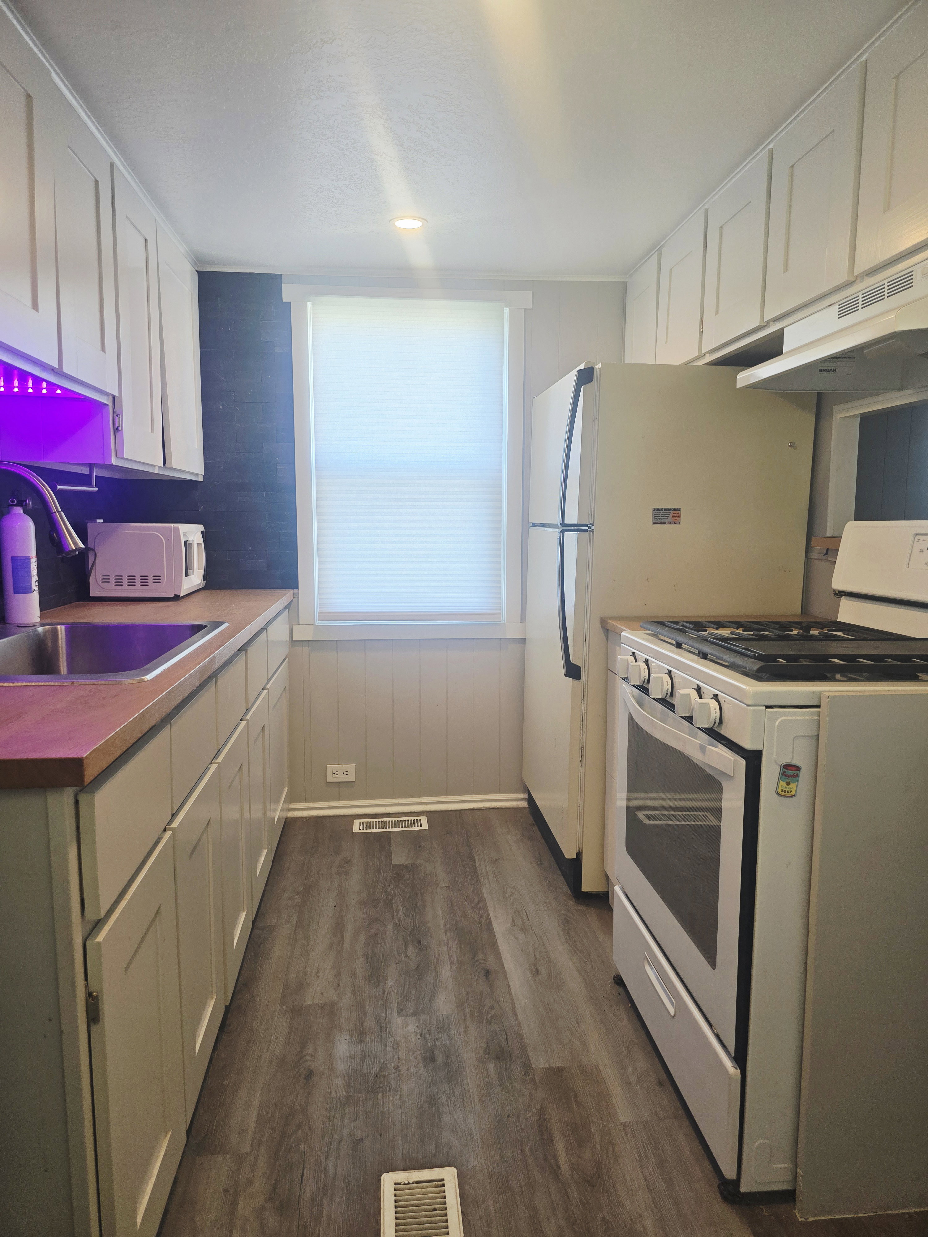 Galley kitchen featuring wood-finish flooring, light-toned cabinetry, and a window with blinds