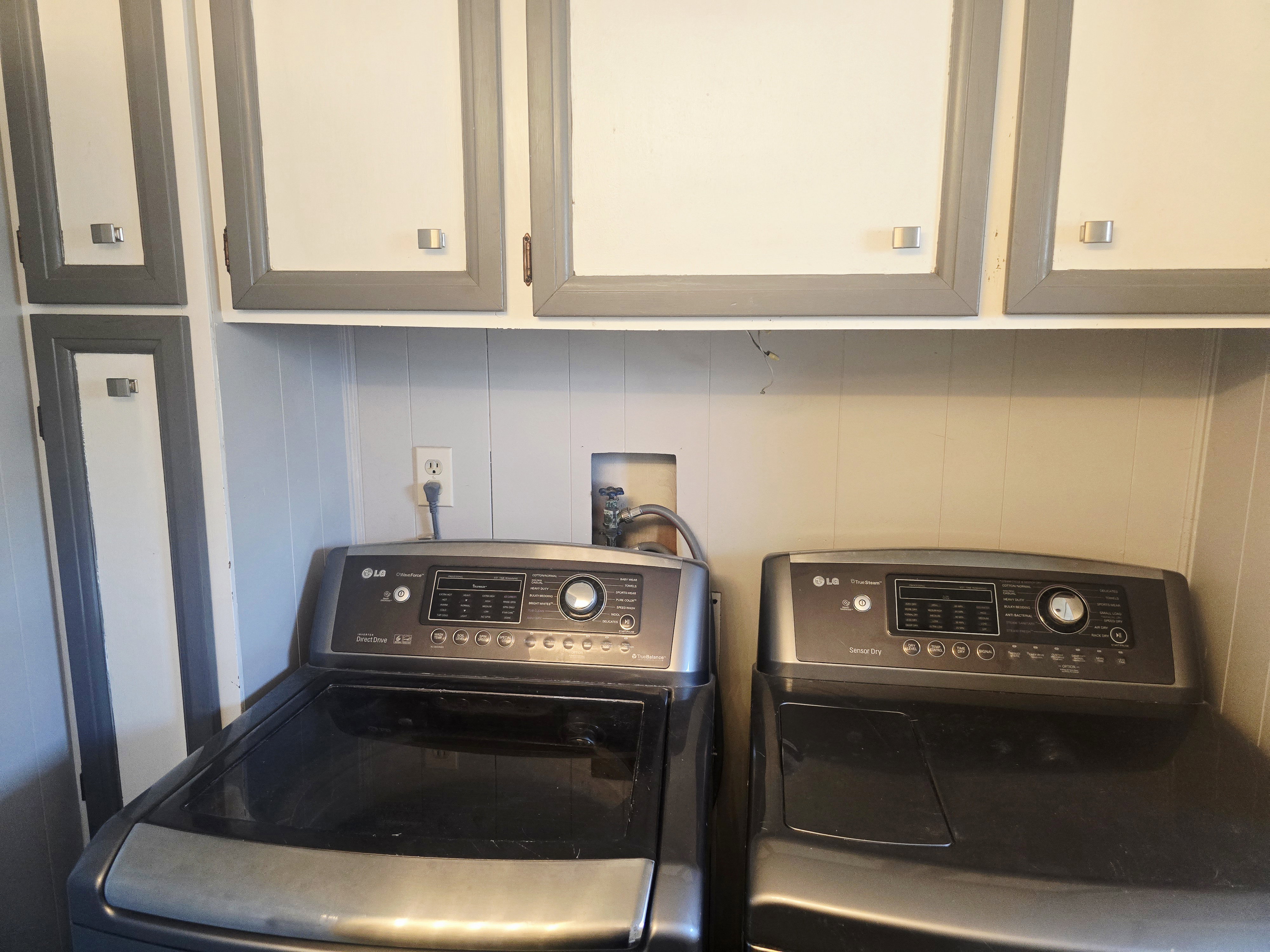 Laundry area featuring white and grey paneled cabinetry with square hardware, white paneled walls, and built-in appliance hookups