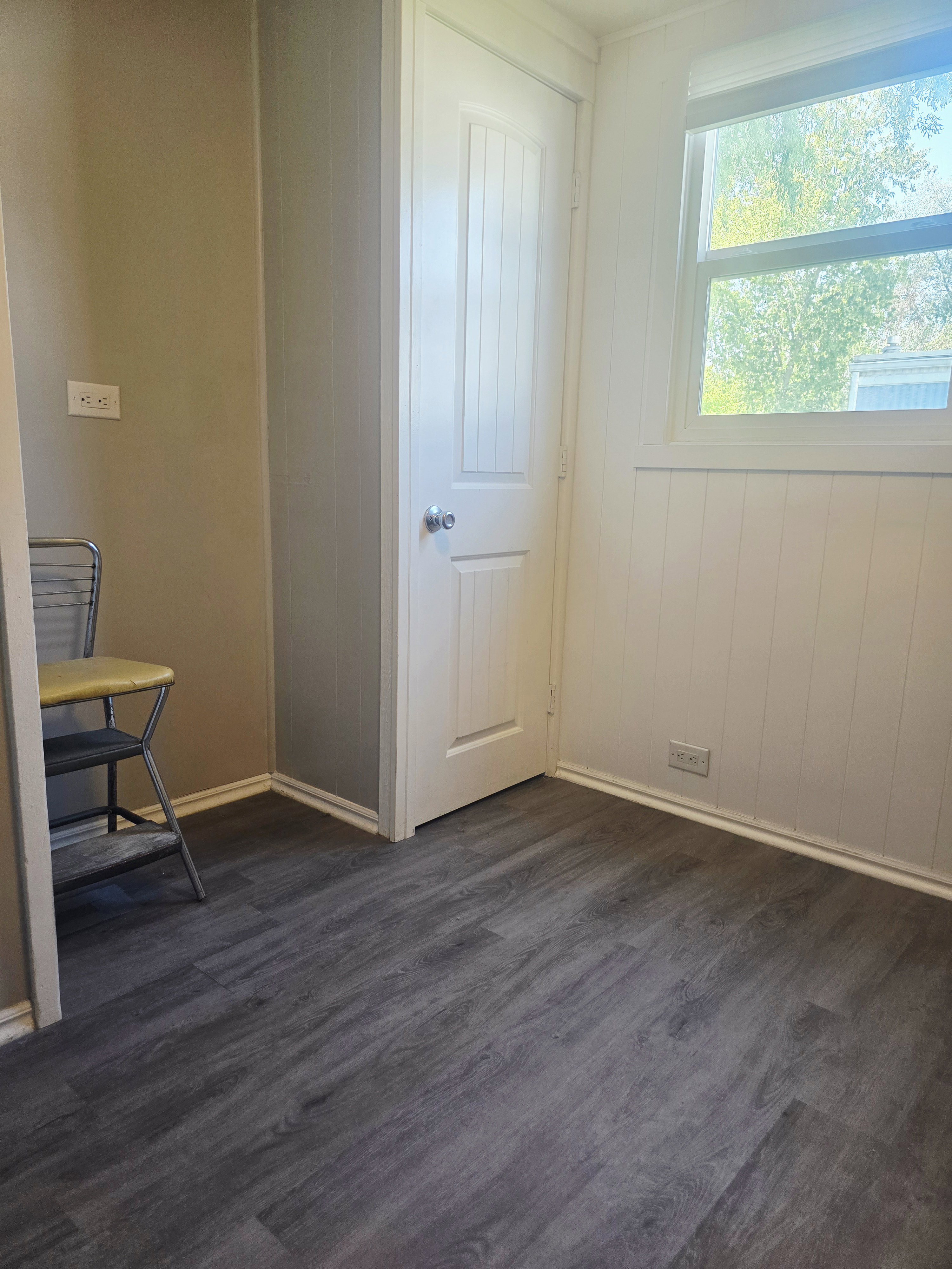Room featuring wood-finish flooring, a white paneled door, and a window providing natural light