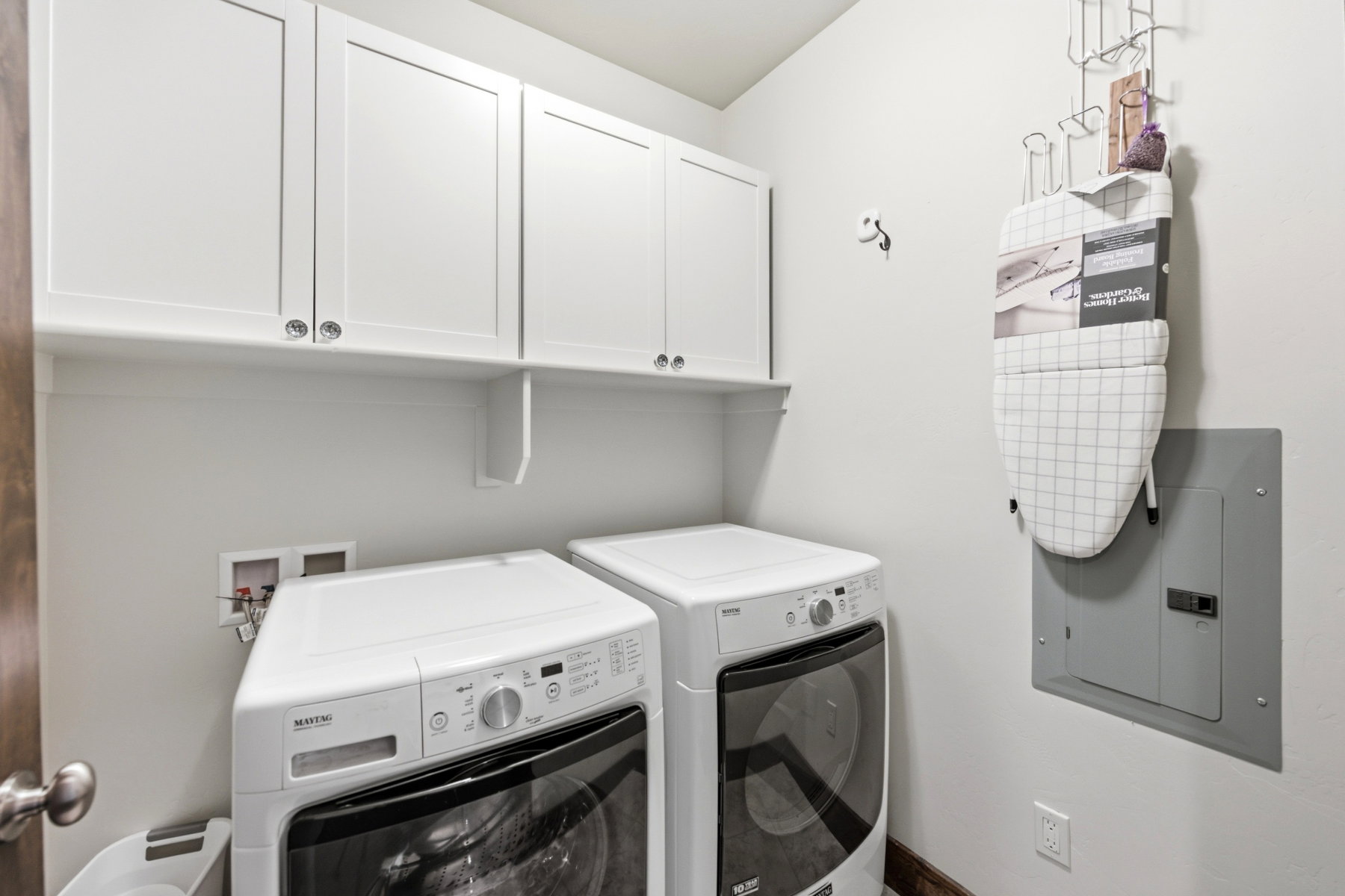 Dedicated laundry area featuring white shaker-style upper cabinetry, a coordinating white wall shelf, and light-toned wall paint