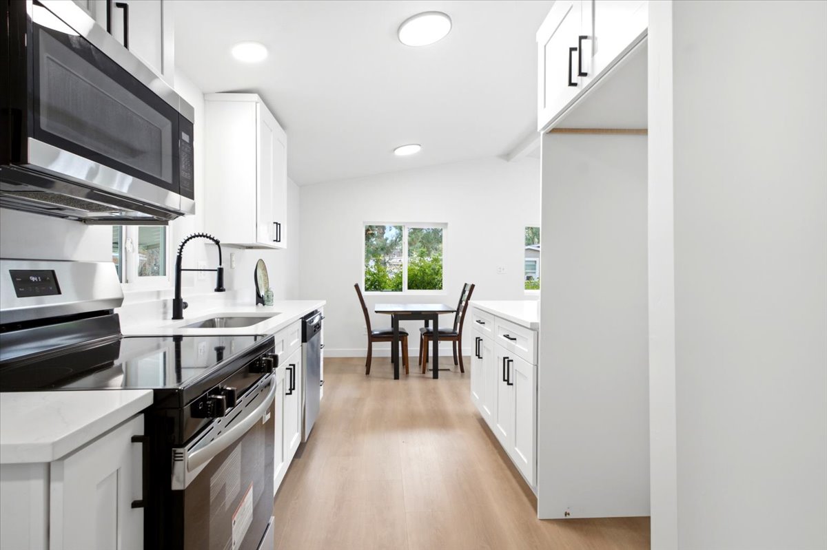 Modern kitchen featuring white shaker cabinetry, stainless steel appliances, quartz countertops, and wood-finish flooring