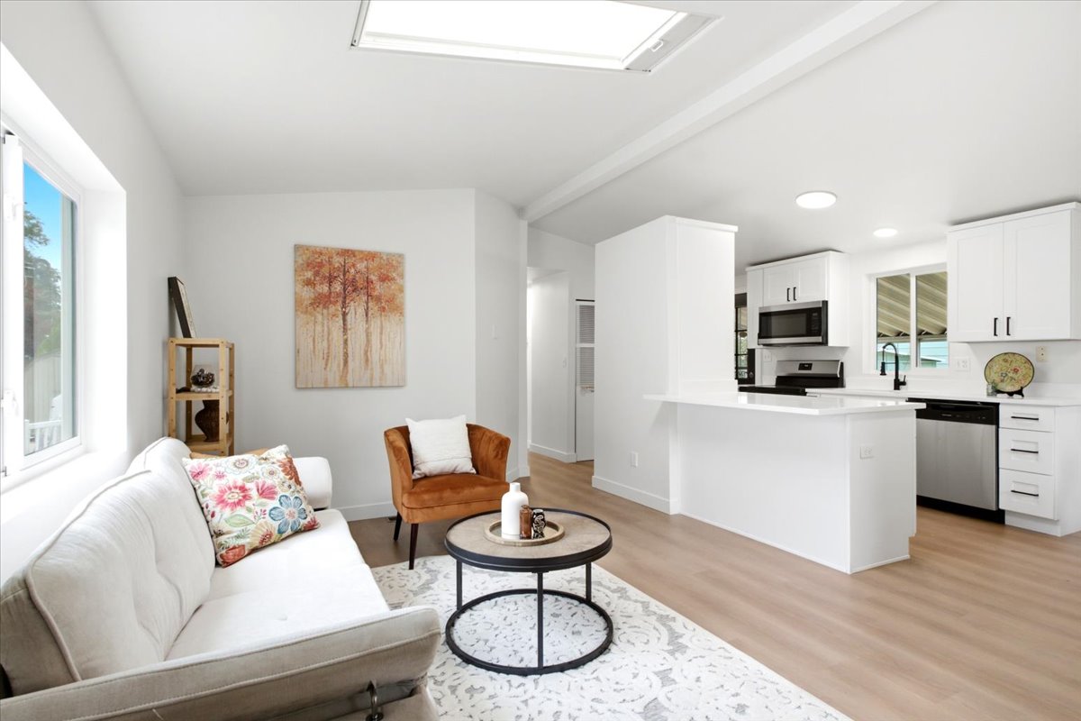 Open-concept living space featuring a skylight, wood-finish flooring, and white walls