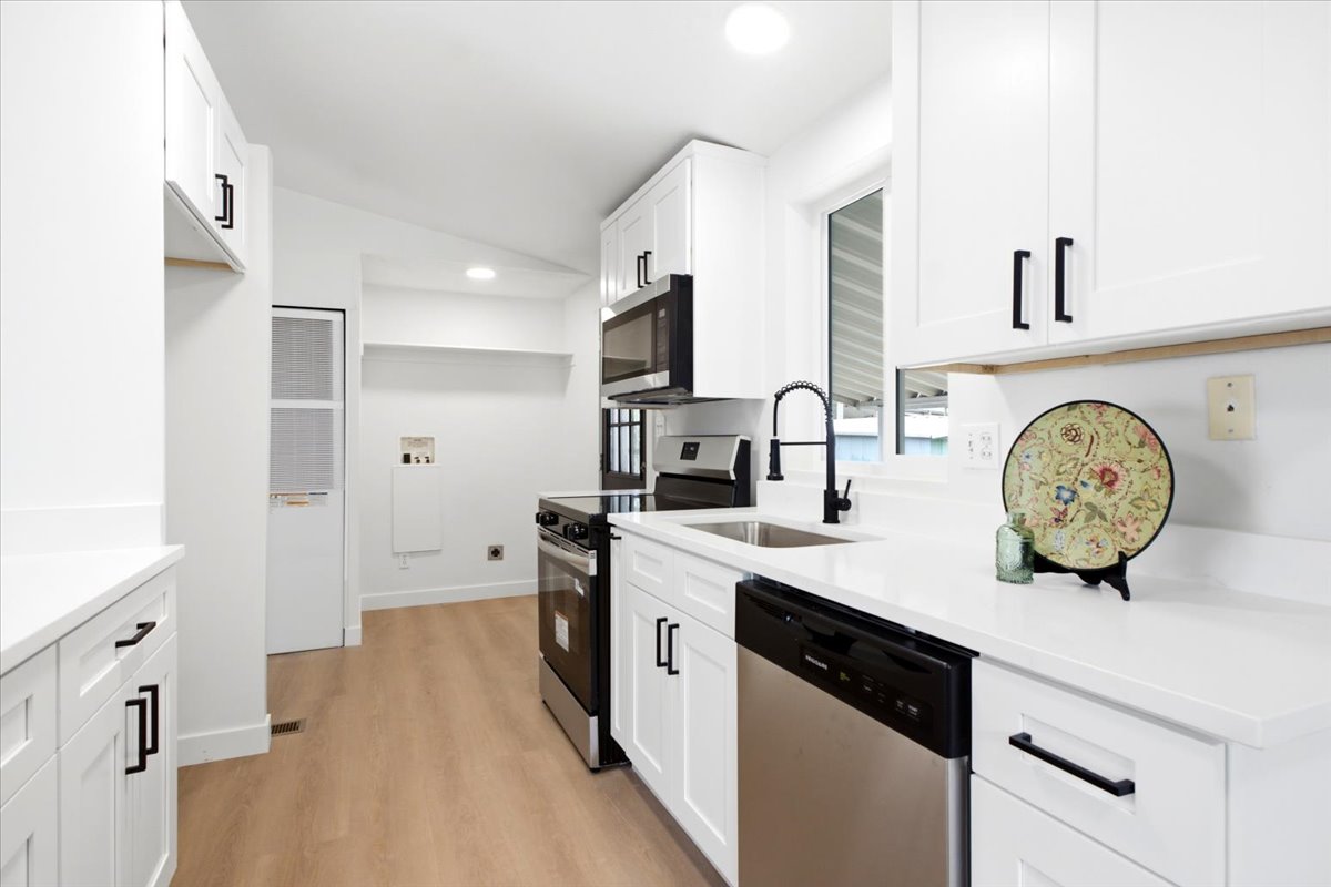 Modern kitchen featuring white cabinetry, stainless steel appliances, light wood-finish flooring, a matte black faucet, and a large window