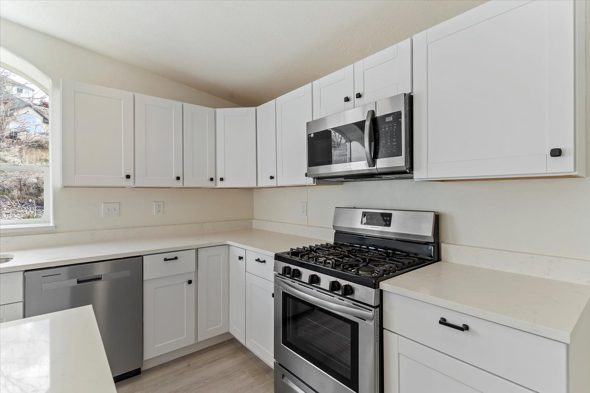 Modern kitchen featuring white shaker-style cabinetry, light-toned countertops, a stainless steel gas range, and a stainless steel built-in microwave