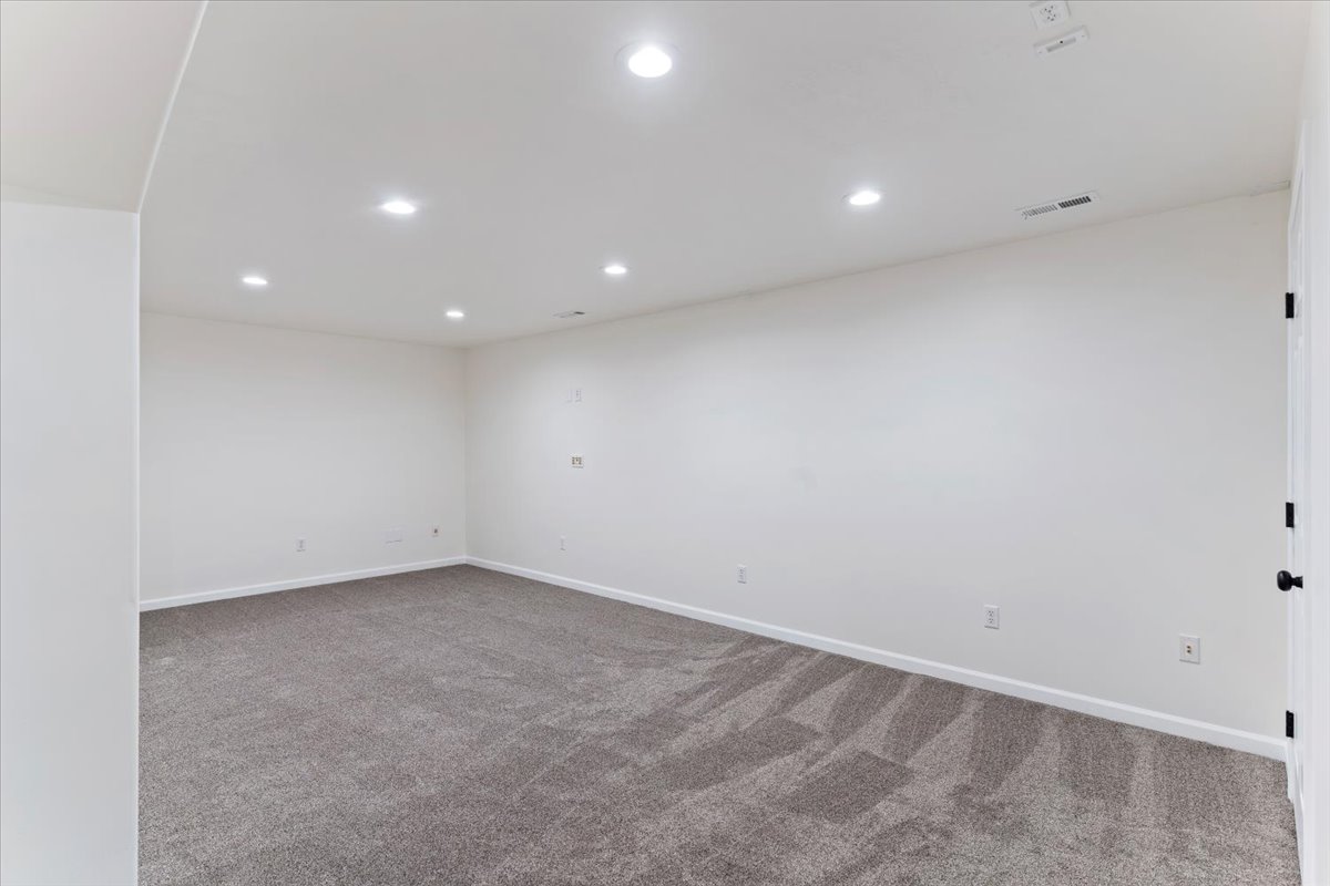 Spacious room featuring neutral carpeting, recessed ceiling lighting, crisp white walls, white baseboards, and a white interior door with matte black hardware
