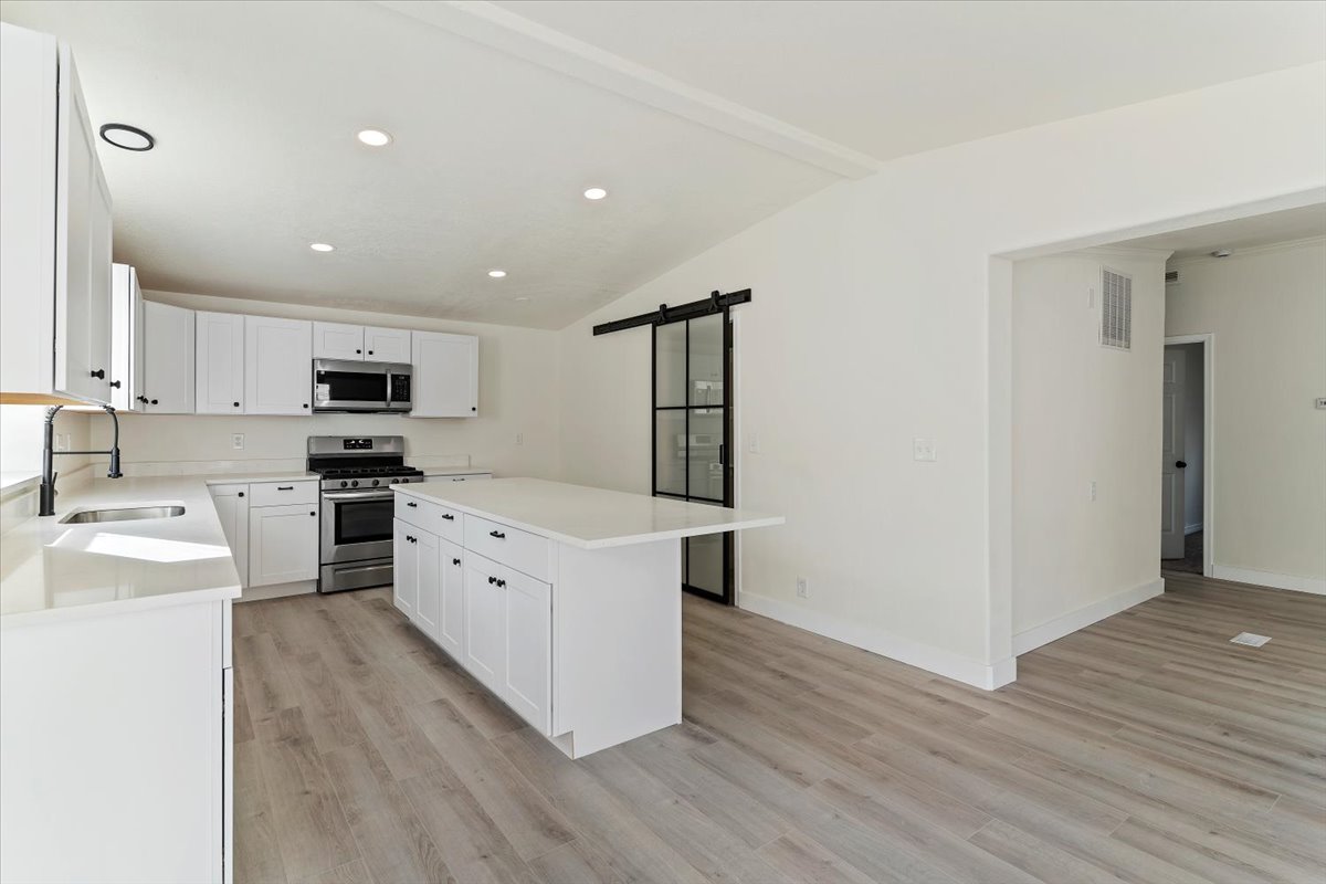 Kitchen featuring white shaker cabinetry, stainless steel appliances, light-toned countertops, and wood-finish flooring