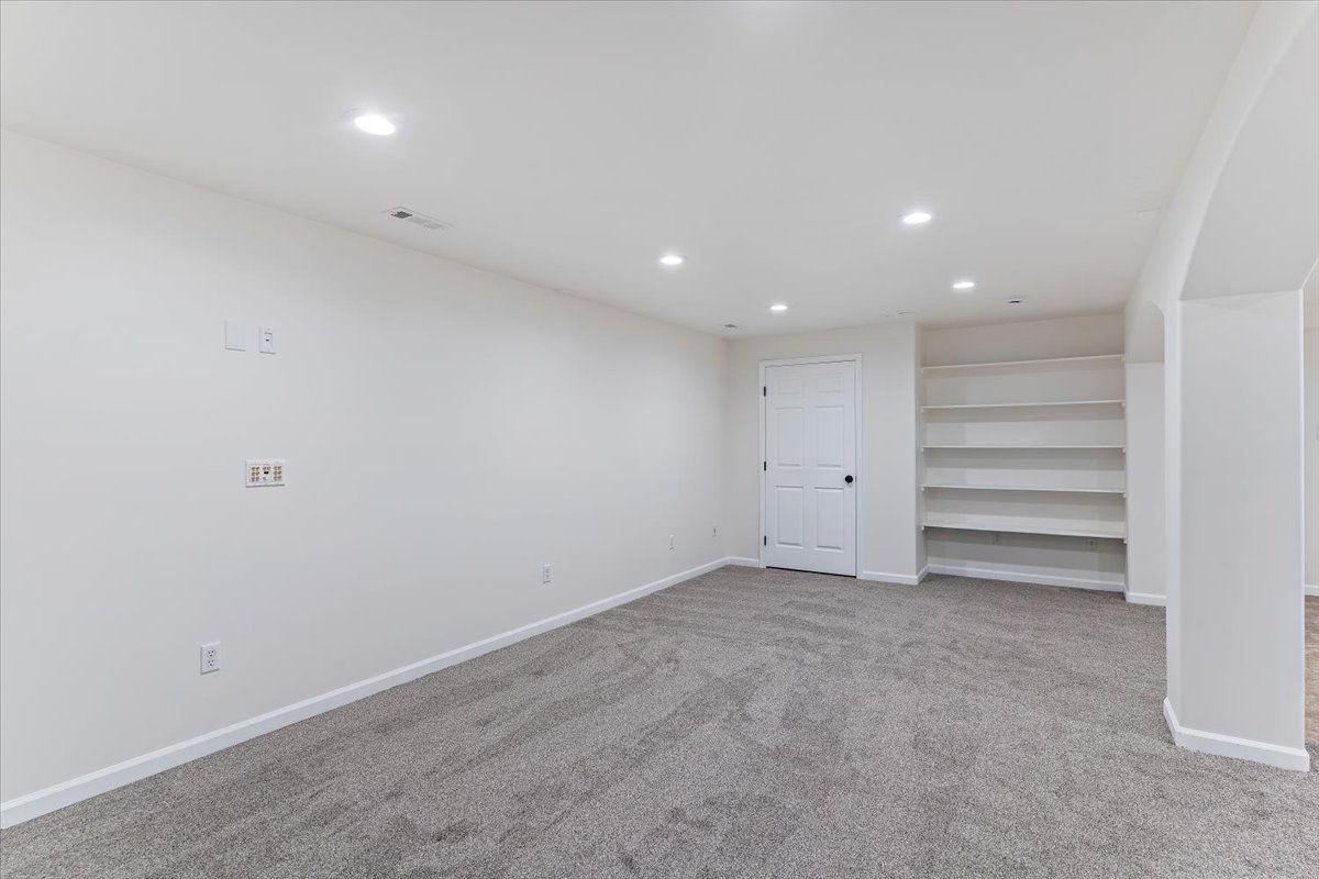Spacious room featuring neutral carpeting, recessed lighting, built-in shelving, a paneled door, and an arched entryway