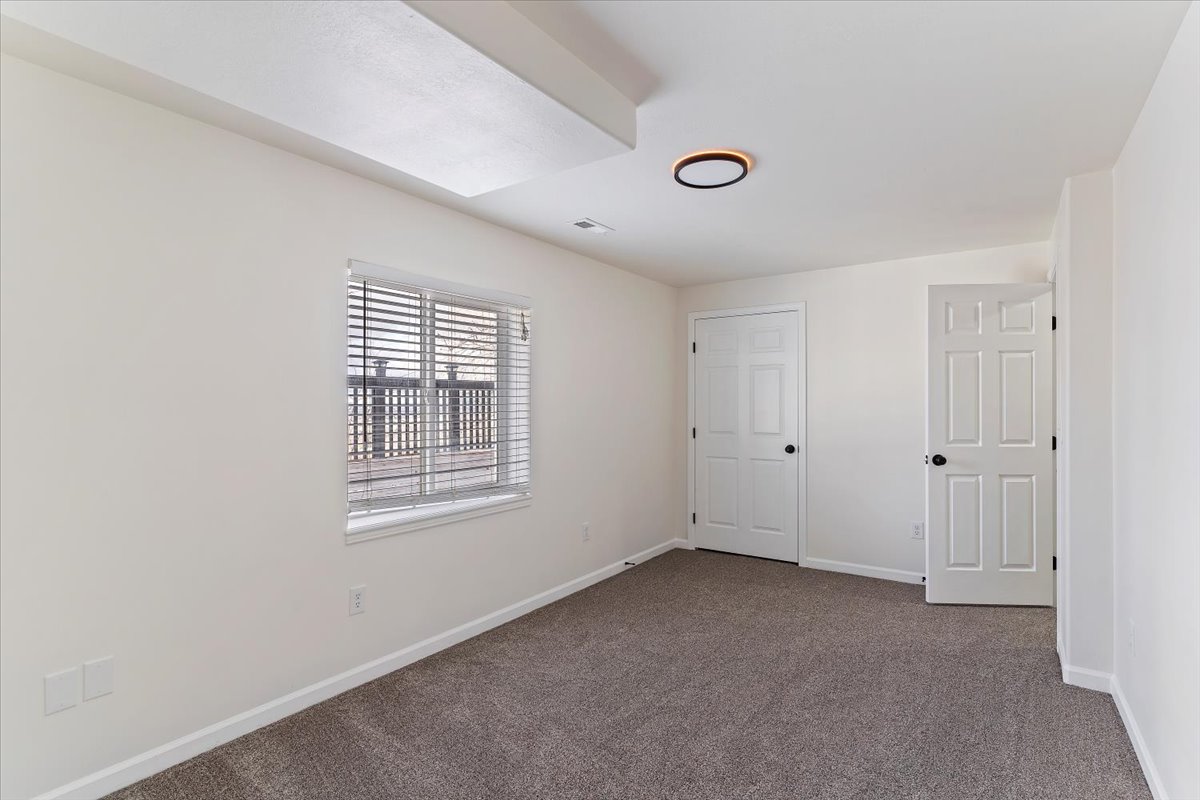 Interior room featuring neutral wall finishes, grey carpet flooring, and a large window with horizontal blinds