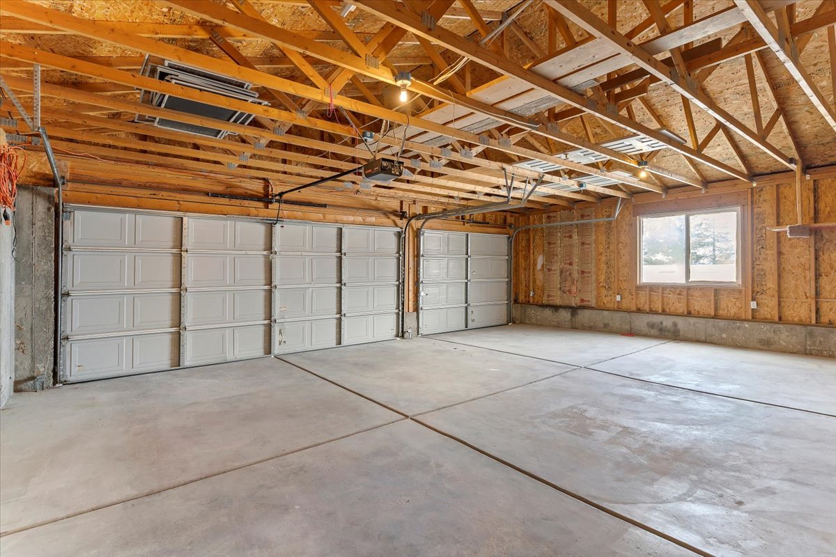 Spacious garage featuring a concrete floor, exposed wood ceiling joists, two panel garage doors, and a double-hung window
