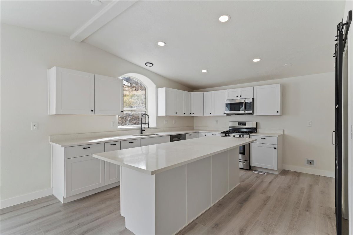 Contemporary kitchen featuring white cabinetry, light-toned countertops, a central island, recessed lighting, and wood-finish flooring